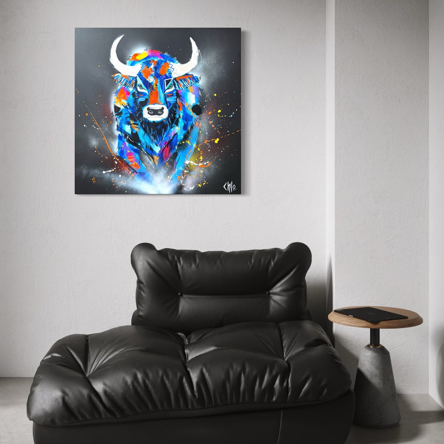Tableau contemporain représentant un taureau coloré et expressif, accroché au mur d’un intérieur moderne et épuré, au-dessus d’un fauteuil en cuir noir, mettant en valeur l’œuvre dans un salon design.