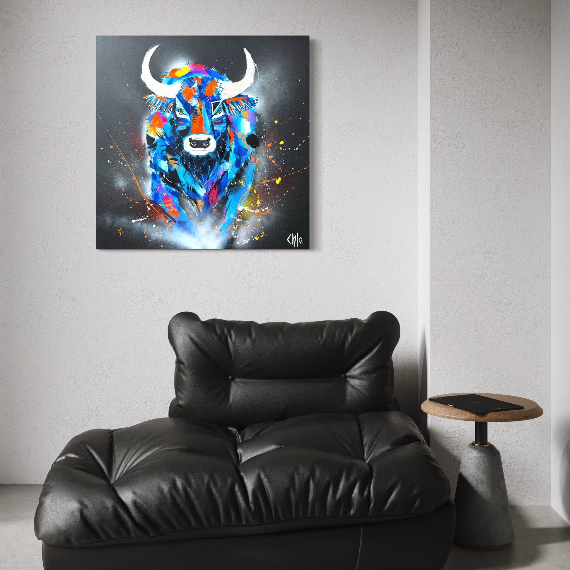 Tableau contemporain représentant un taureau coloré et expressif, accroché au mur d’un intérieur moderne et épuré, au-dessus d’un fauteuil en cuir noir, mettant en valeur l’œuvre dans un salon design.